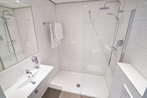 Amrâth Hotel Lapershoek Arenapark ruime badkamer met witte meubels, een wastafel, toilet en een inloopdouche.