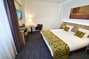 Amrâth Hotel Lapershoek Arenapark Comfort kamer groot tweepersoonsbed met een bewerkt geel sprei en bijpassende kleine kussentjes. 