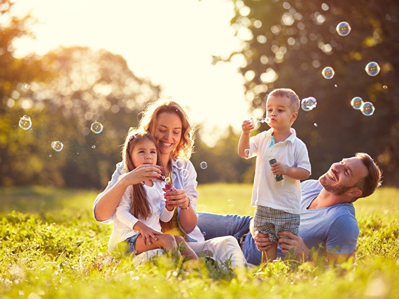 Blije familie speelt met zeepbellen in het park, genietend van een zonnige dag samen.