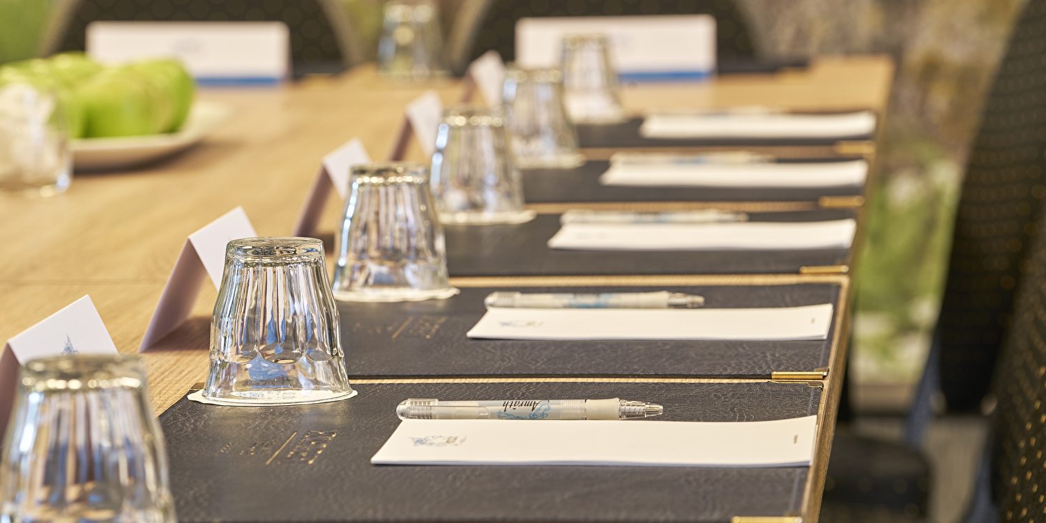 Amrâth Hotel Lapershoek Arenapark, een vergaderzaal met een lange tafel met meerdere stoelen en een glas water erop geplaatst.