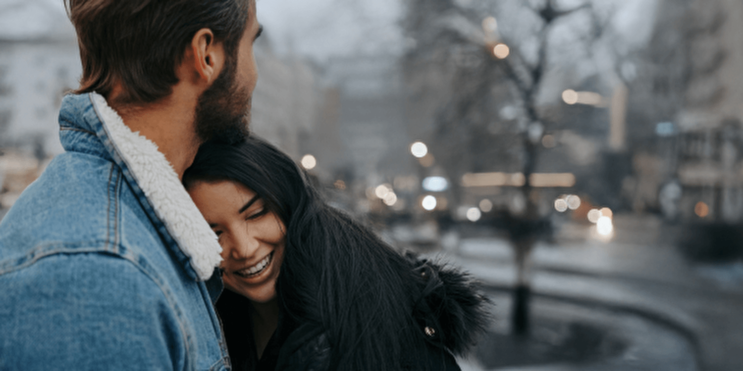 A man and woman stand in the rain and embrace each other, their love visible despite the bad weather.